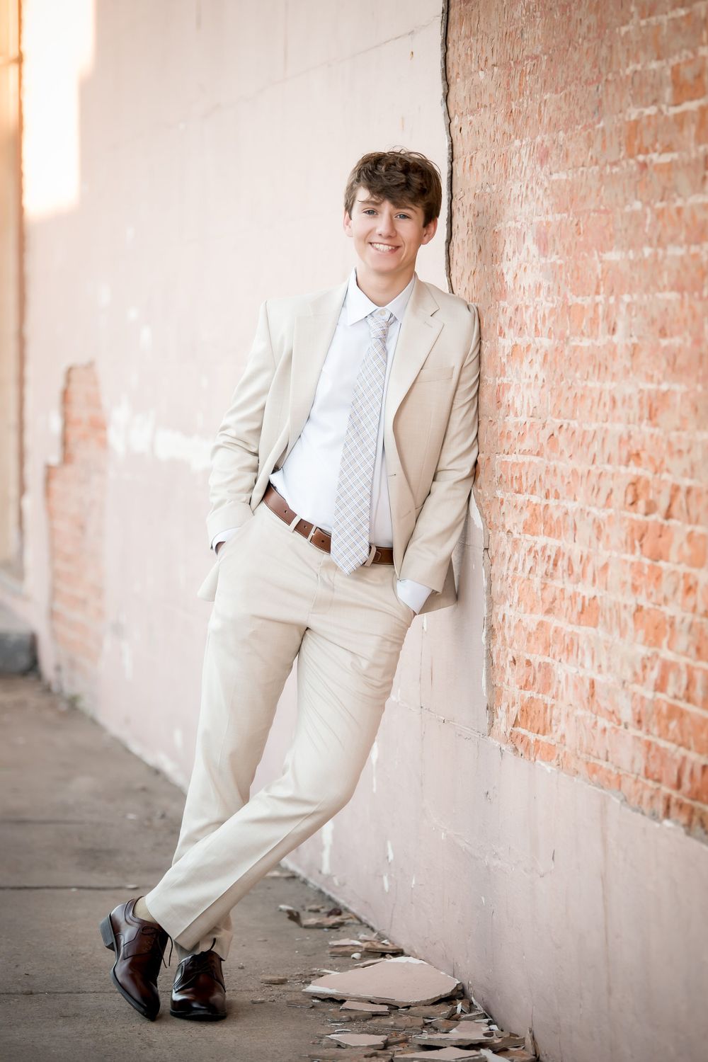 Casual portrait against brick wall showing person in beige suit with hands in pockets.