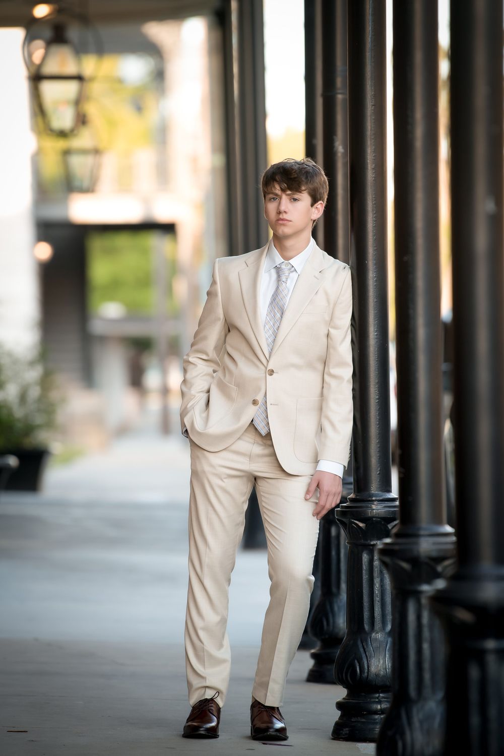 Urban portrait featuring person in beige suit walking past classic black columns and street lamps.