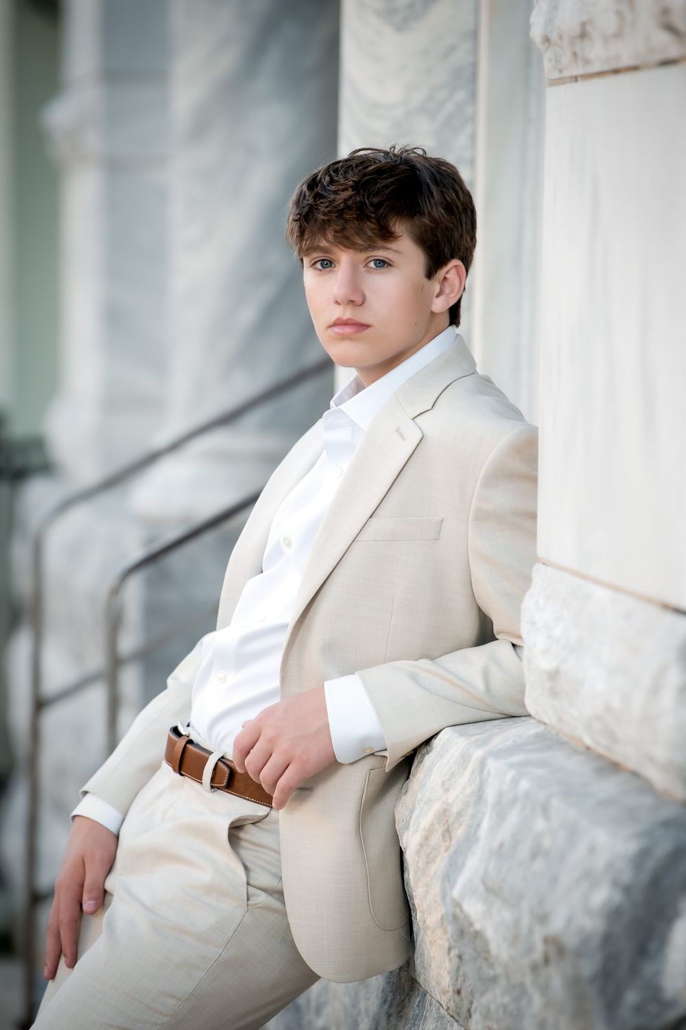 Formal portrait of a person in cream colored suit sitting on stone steps.