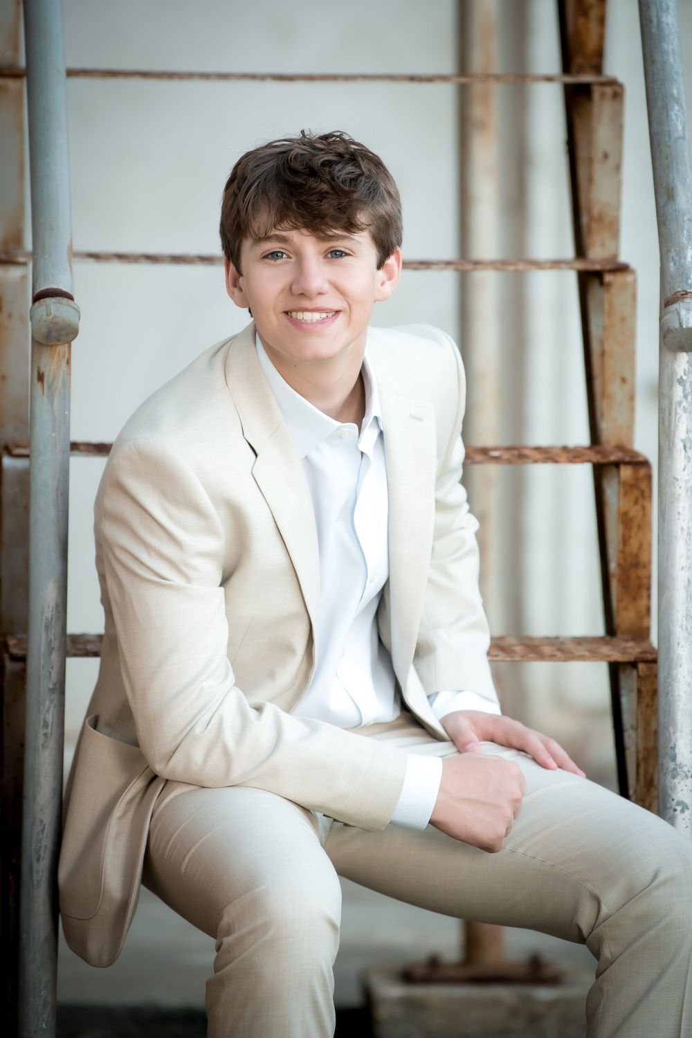 Portrait of a person in light colored suit sitting on industrial metal steps.