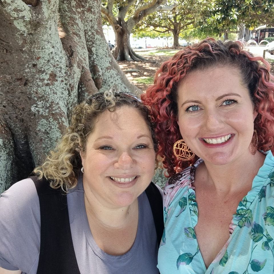 Two friends taking selfies together outdoors showing warm smiles and genuine expressions of joy.