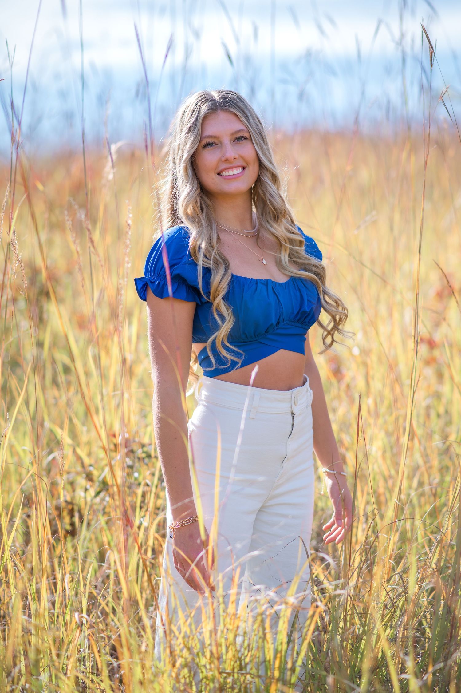 A woman in a blue crop top poses in a golden wheat field on a sunny day.