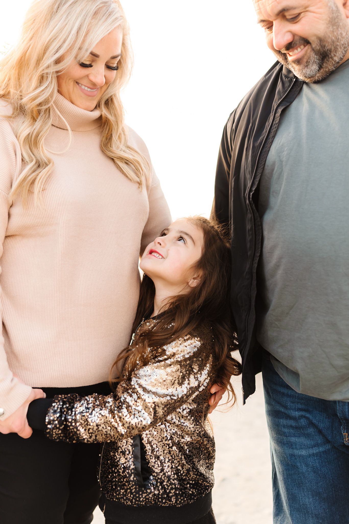 Family portrait with sparkly gold dress and neutral tones against white background.