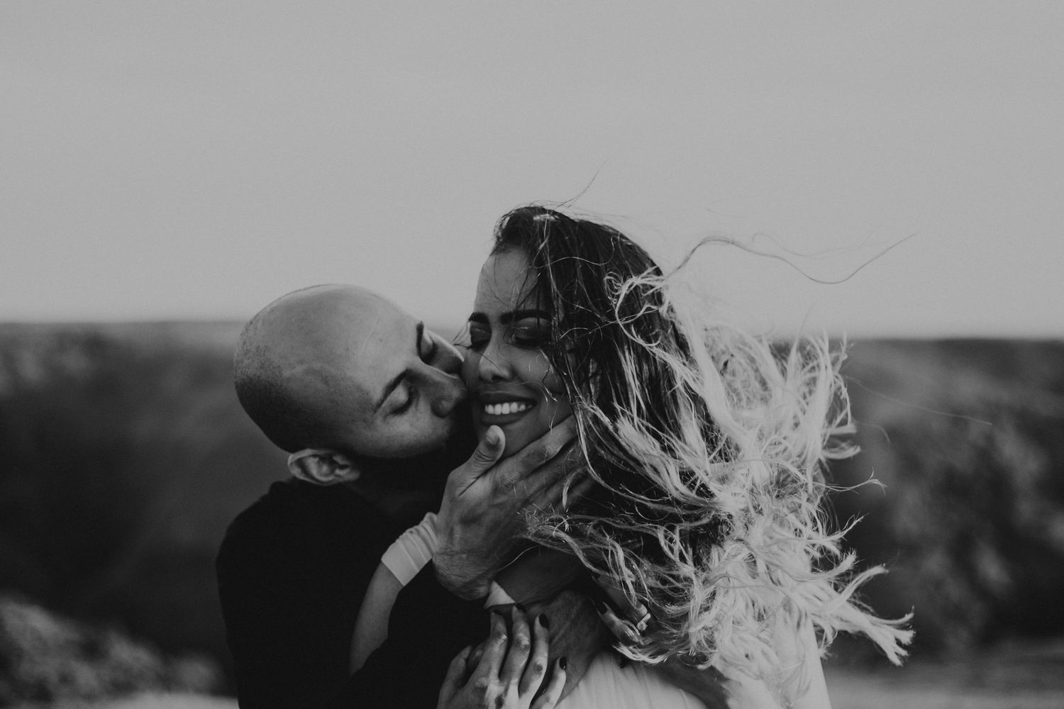 Man kisses wife on the cheek as wind blows her hair