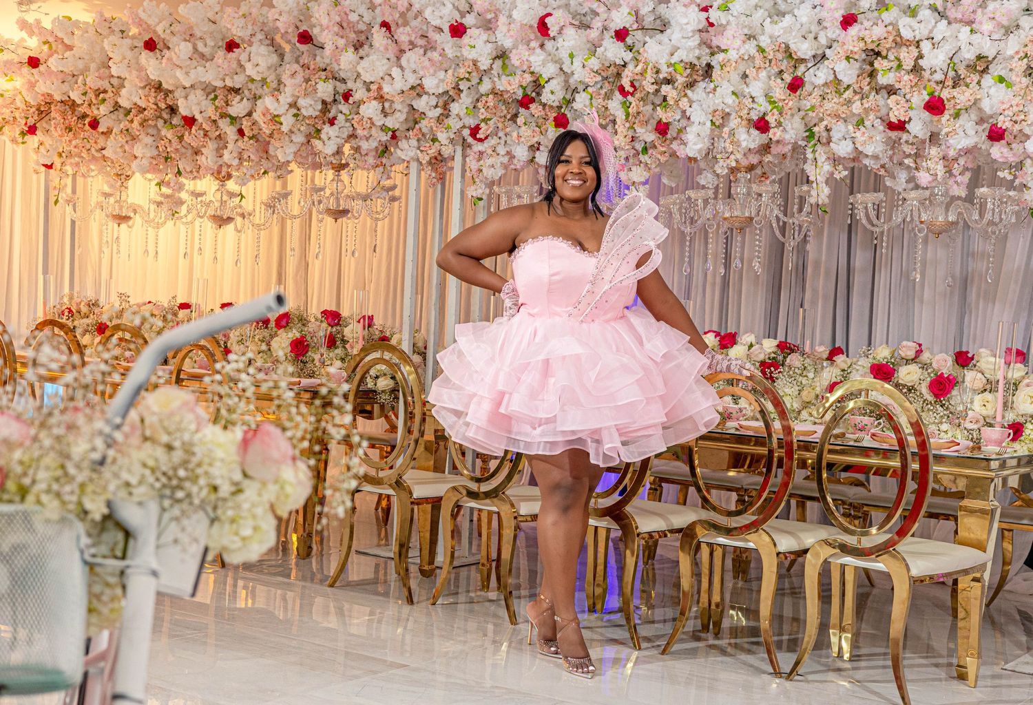 Woman in pink ruffled mini dress posing in elegantly decorated floral event venue.