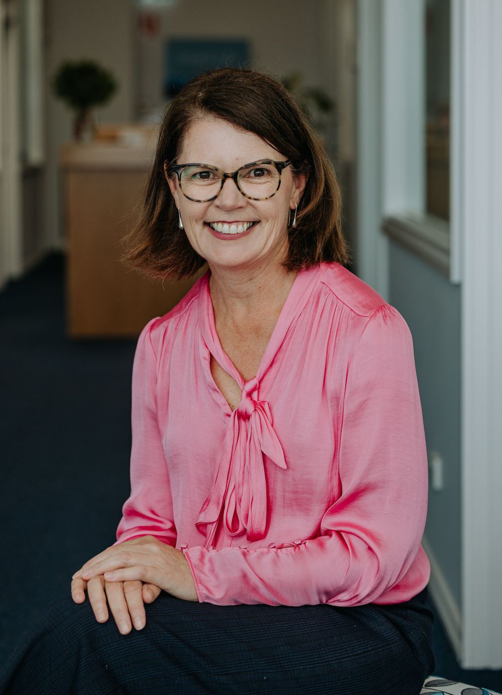 Person wearing pink blouse and glasses sitting at desk in professional setting.