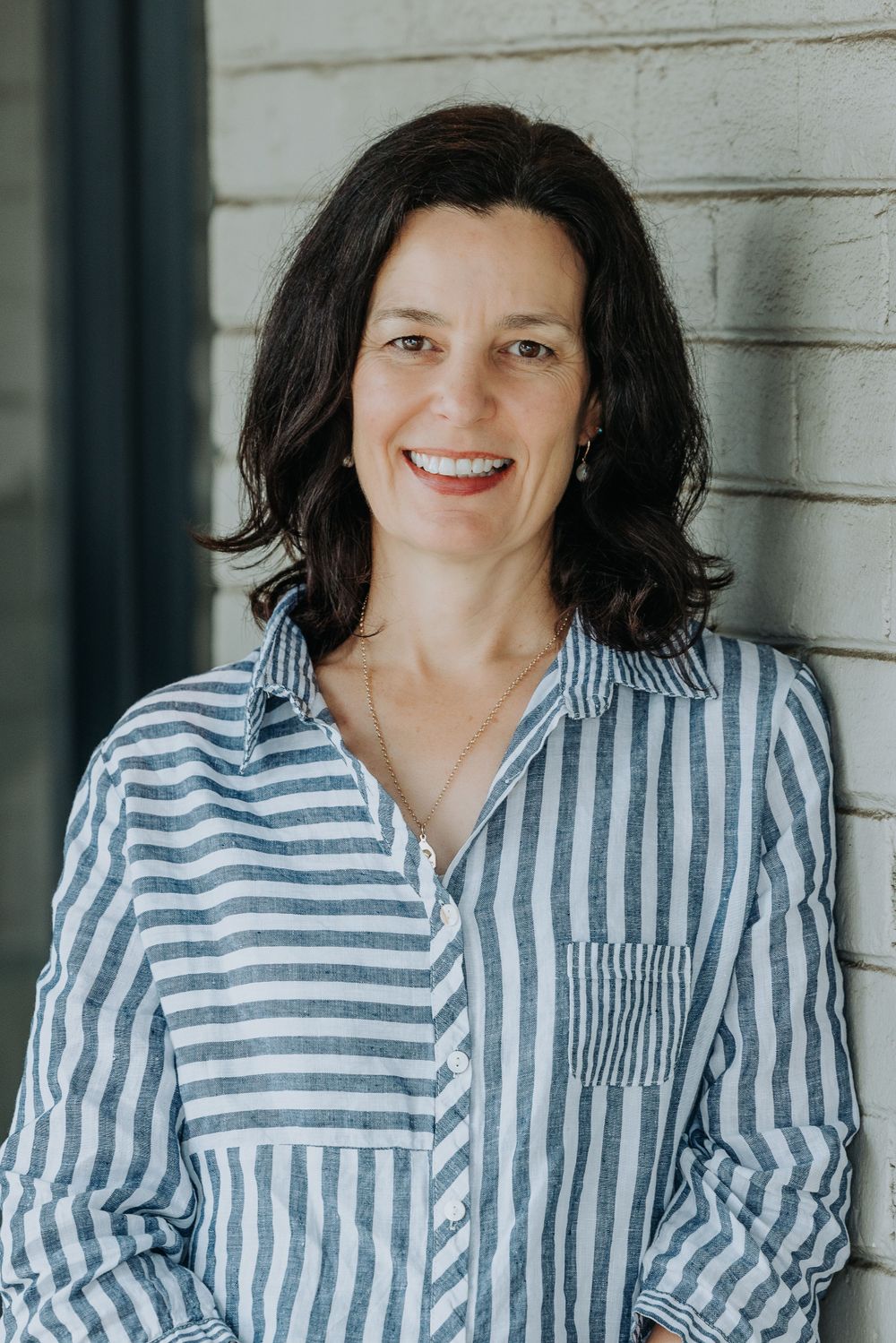 Person wearing striped button-up shirt against white wall background.