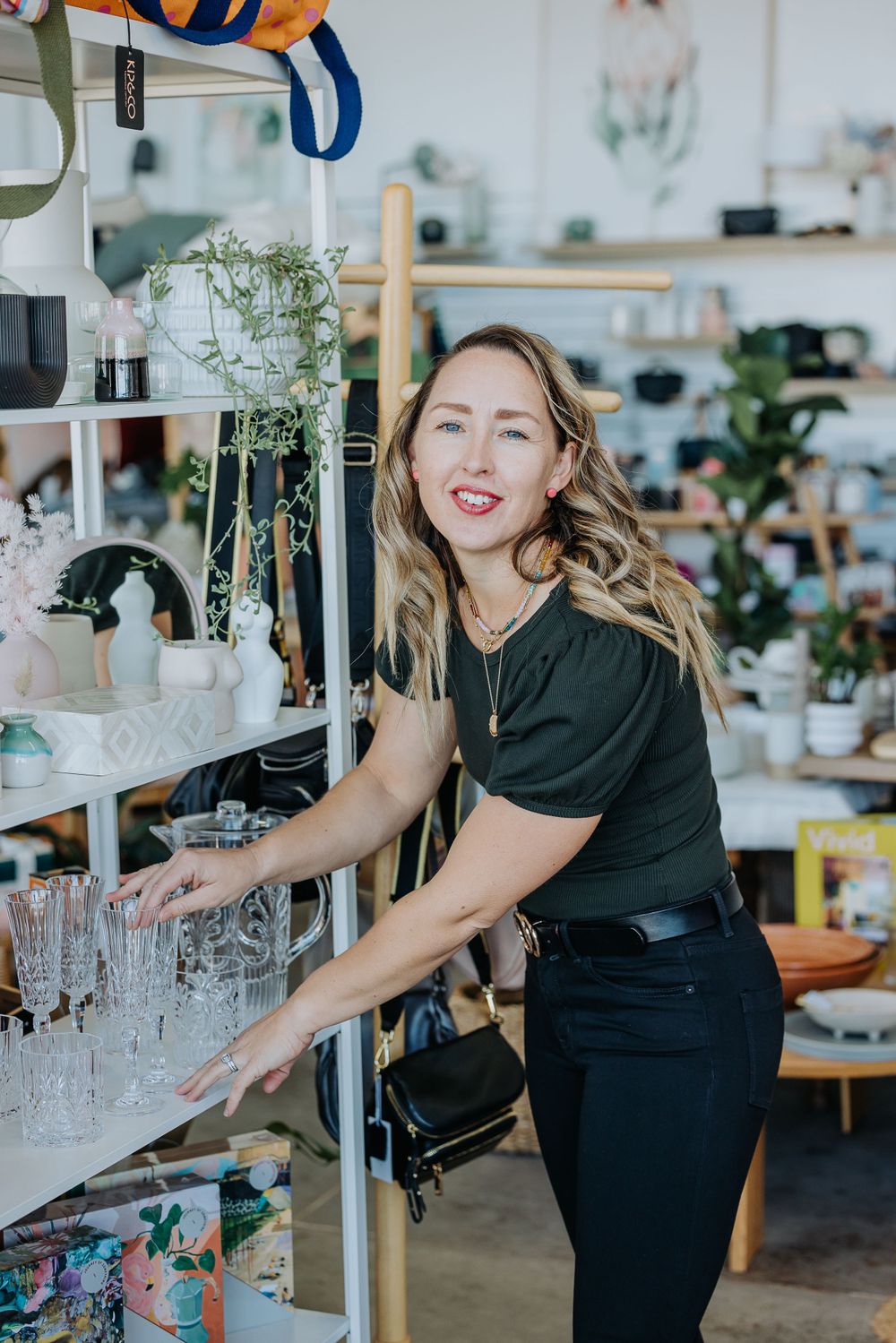 Person in black arranging glassware displays in a retail shop setting.