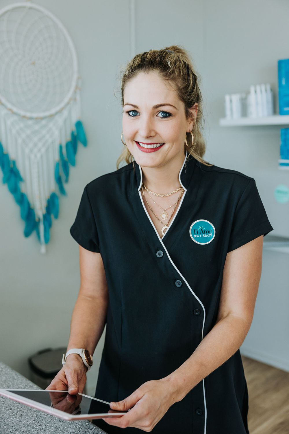 Healthcare professional in black uniform smiling while using a tablet in a medical office.