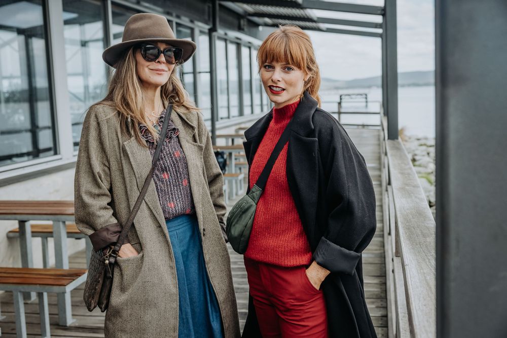 People in stylish winter coats walking and chatting along an urban waterfront.