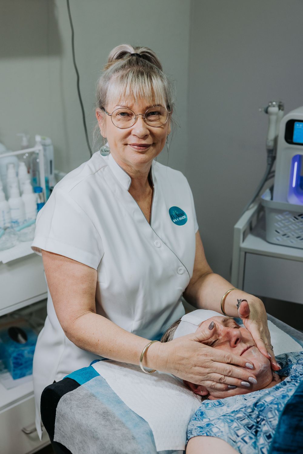 Healthcare worker in white uniform performing a facial treatment in a spa setting.