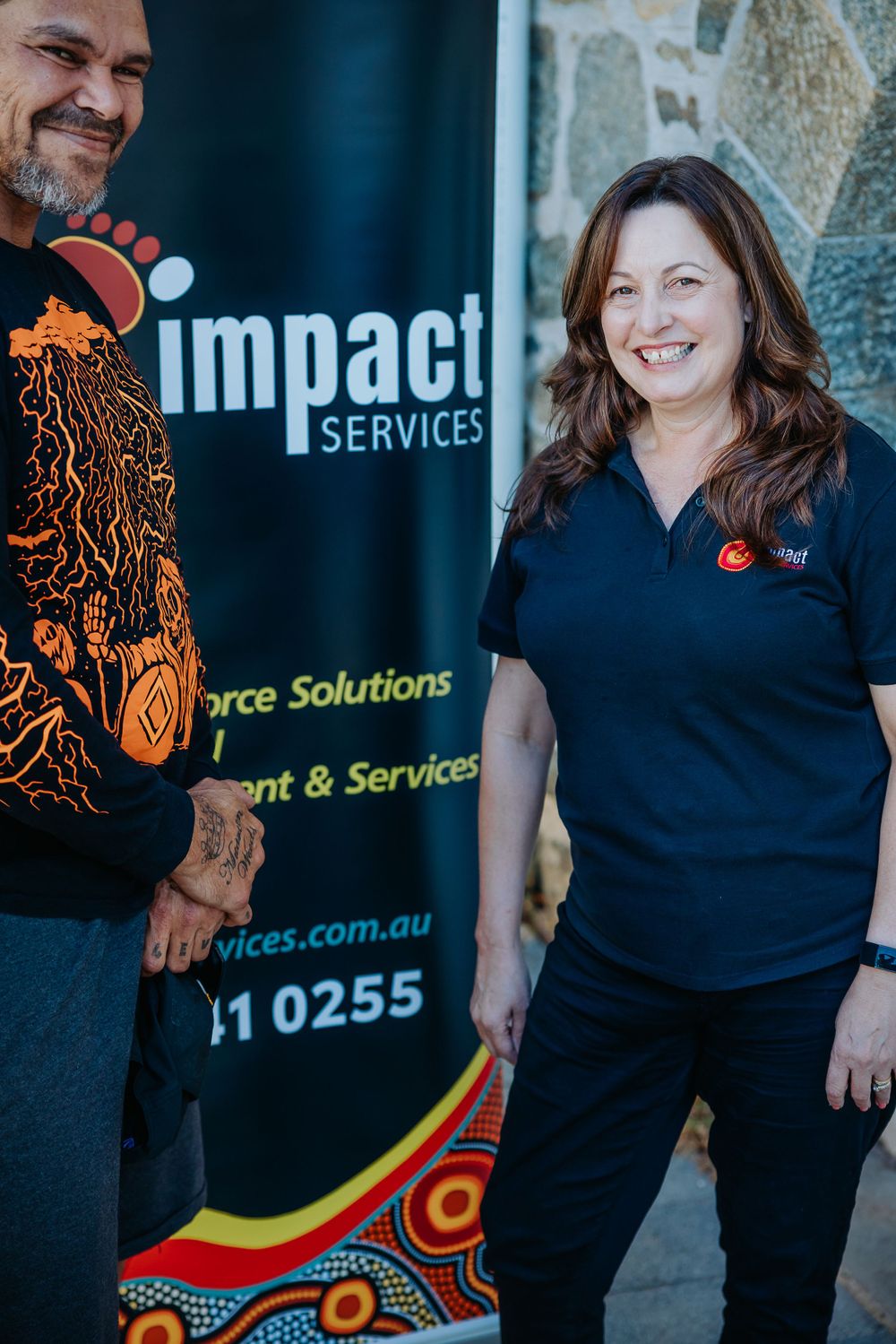 Professional wearing a navy blue polo shirt with Aboriginal-inspired design elements against a corporate backdrop.