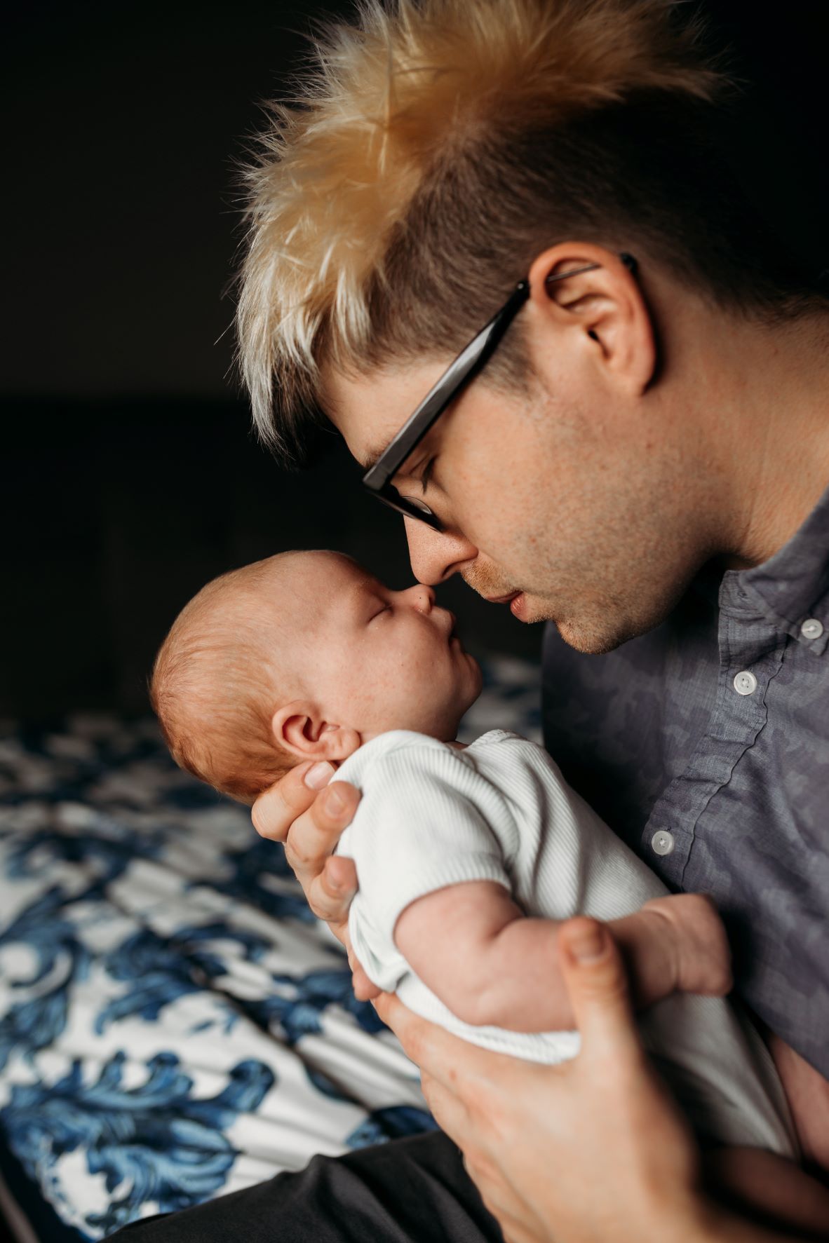 Father with glasses holding newborn and touching noses, both have eyes closed in an emotional tender moment