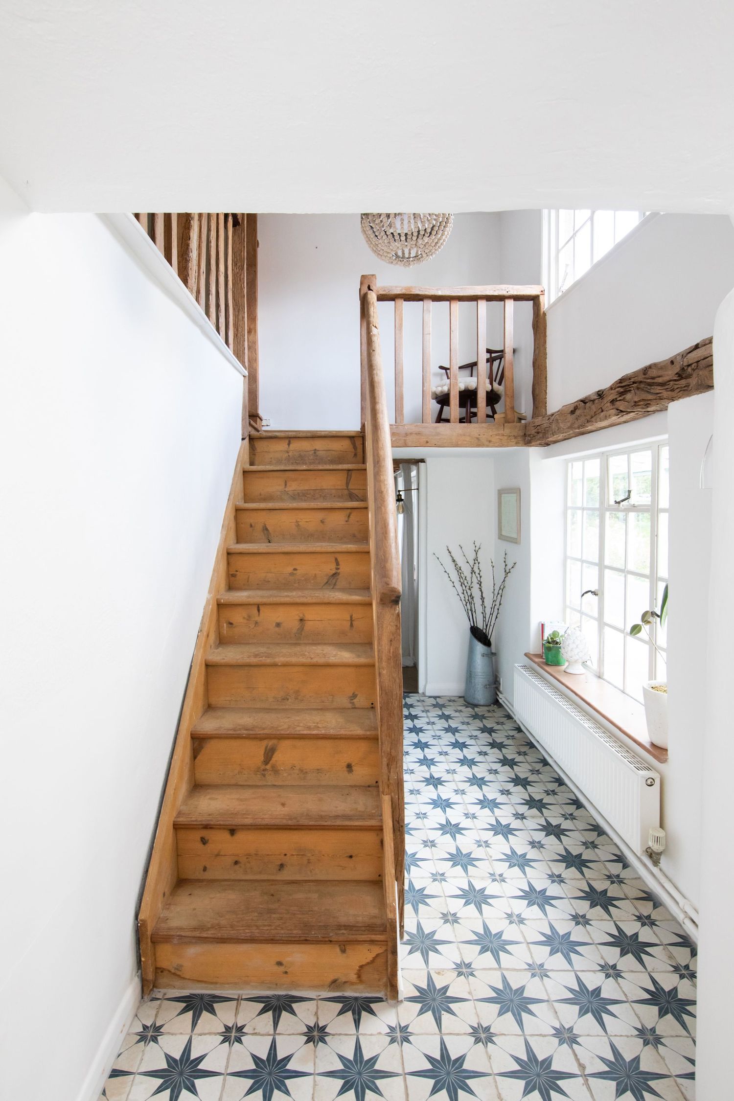 Modern hallway featuring wooden stairs and blue patterned tile flooring with white walls and natural lighting.