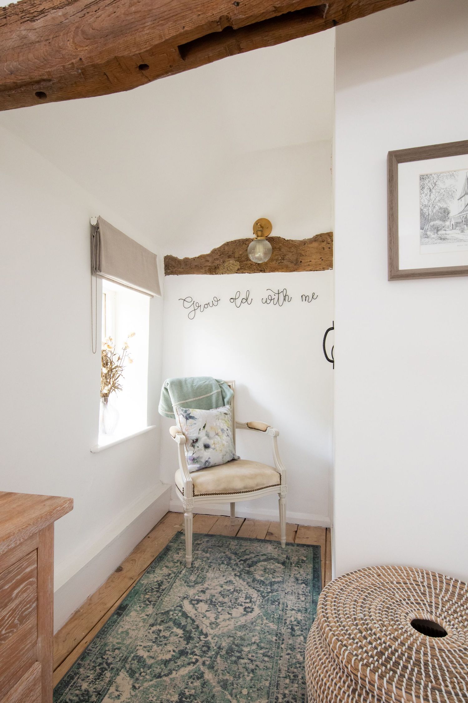 Cozy reading nook with vintage chair, teal rug, and exposed wooden beam overhead.