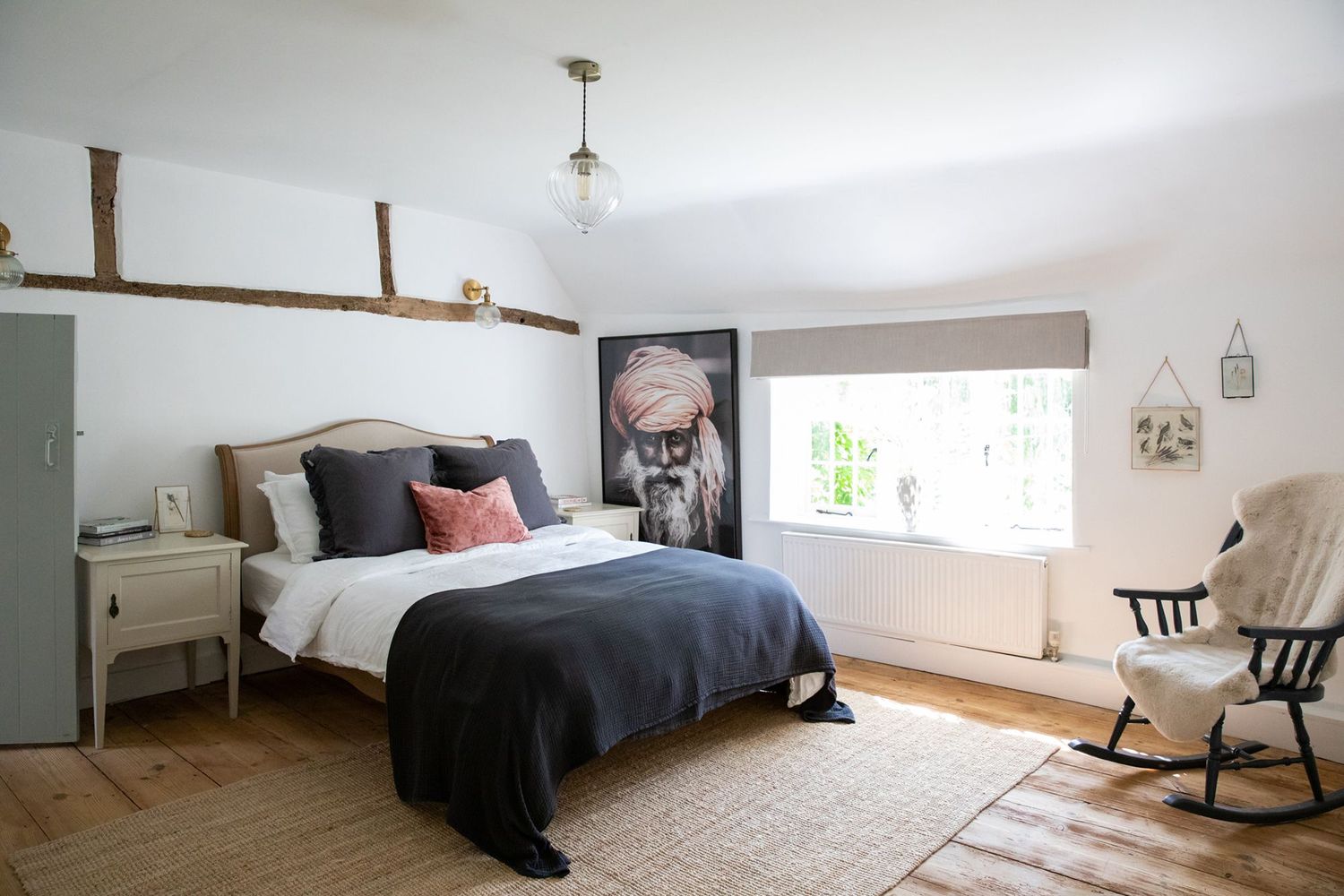 Spacious bedroom with exposed timber beams, navy bedding, and natural hardwood floors.