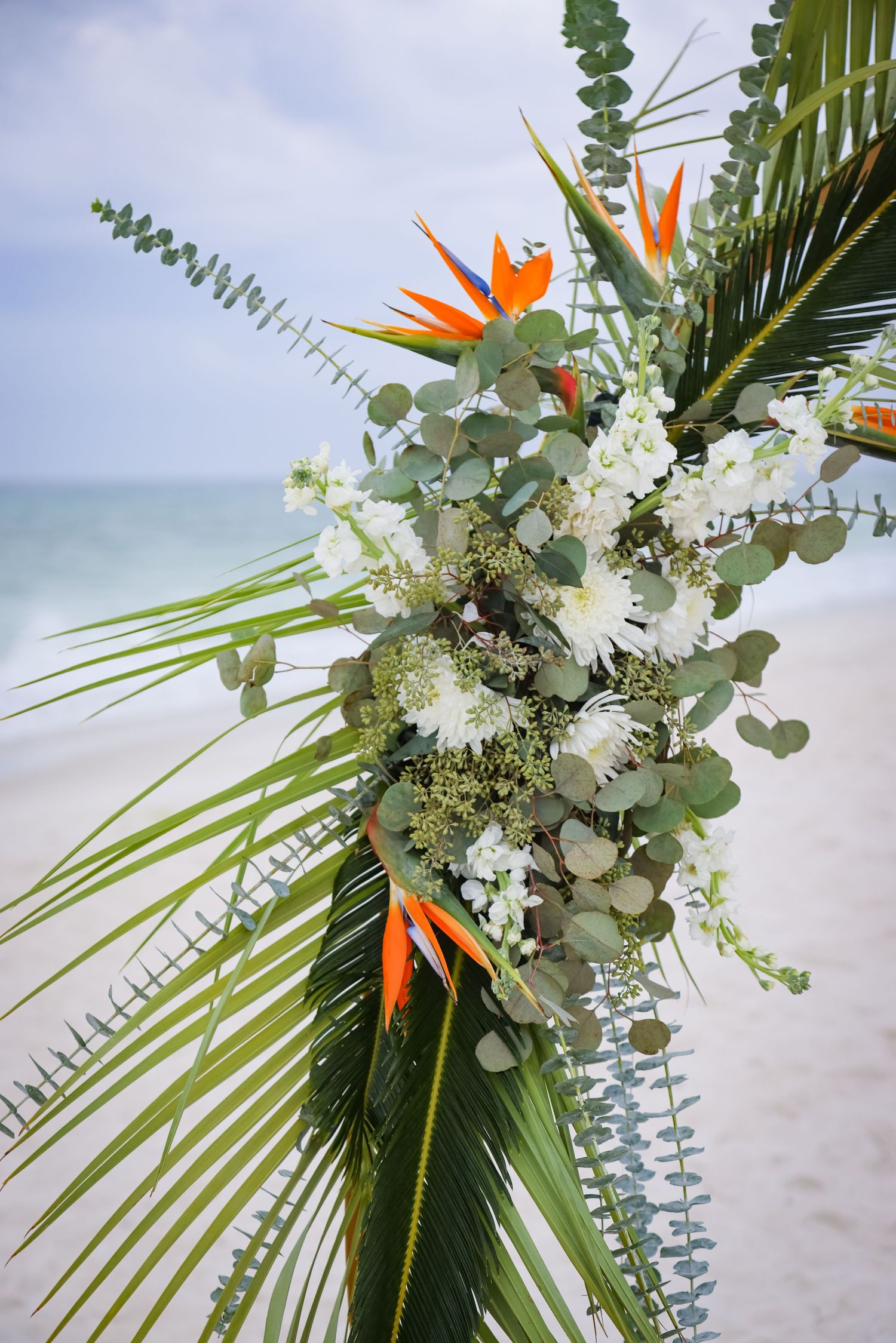 Tropical beach wedding floral arrangement with birds of paradise and white flowers on palm fronds.