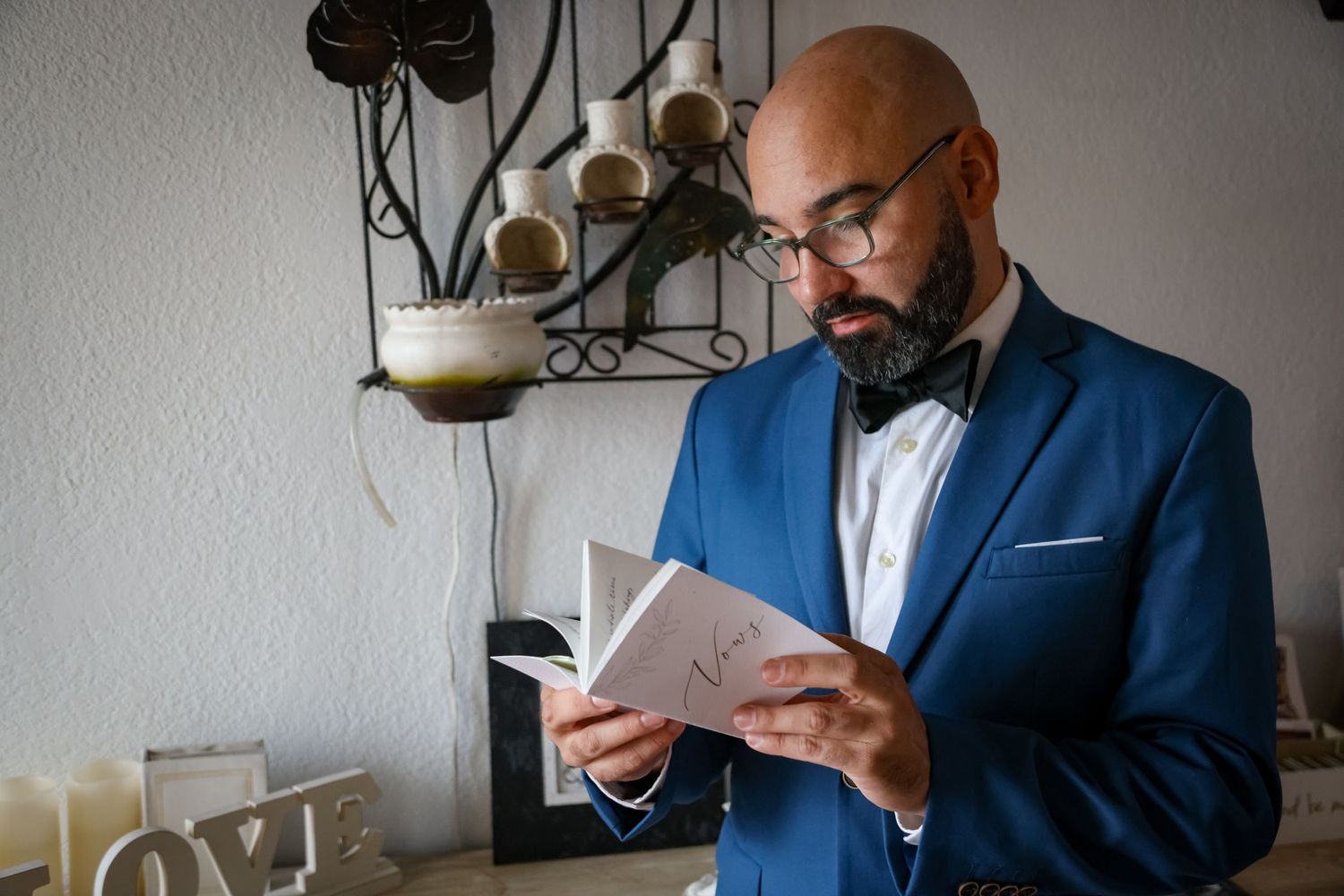 A man in a blue suit reads from a small book in an indoor setting.
