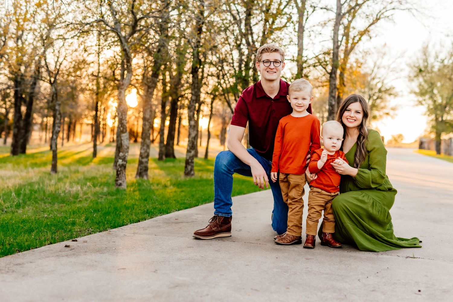 Family portrait on a tree-lined path during golden hour sunset.