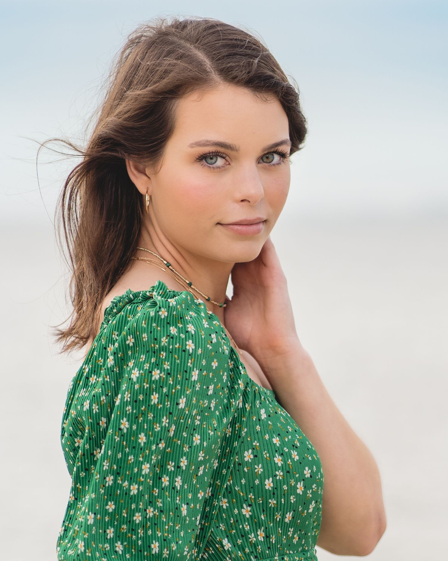 Portrait in green floral dress against soft blue sky background.