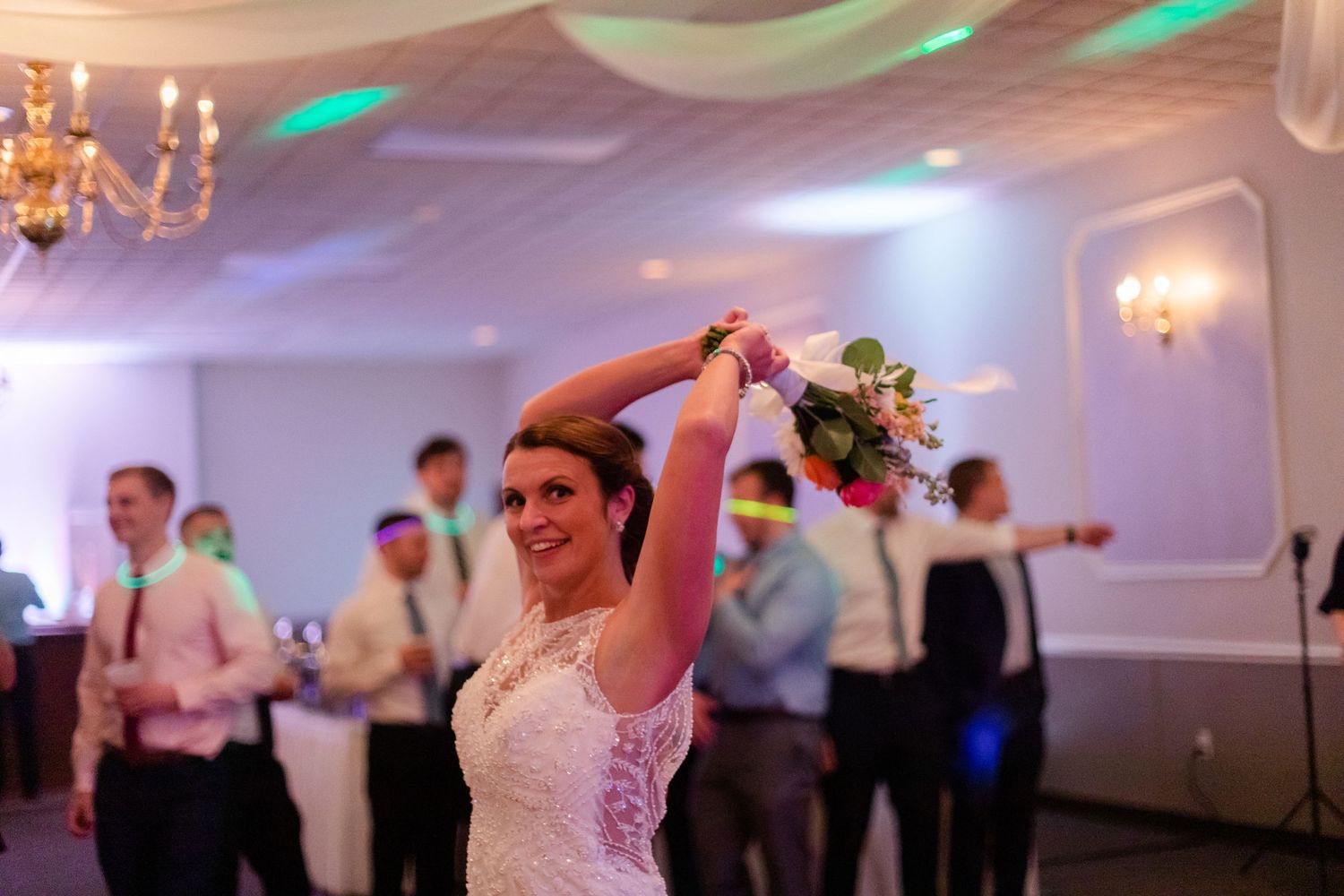Wedding reception dance floor illuminated with colorful lights and chandeliers.