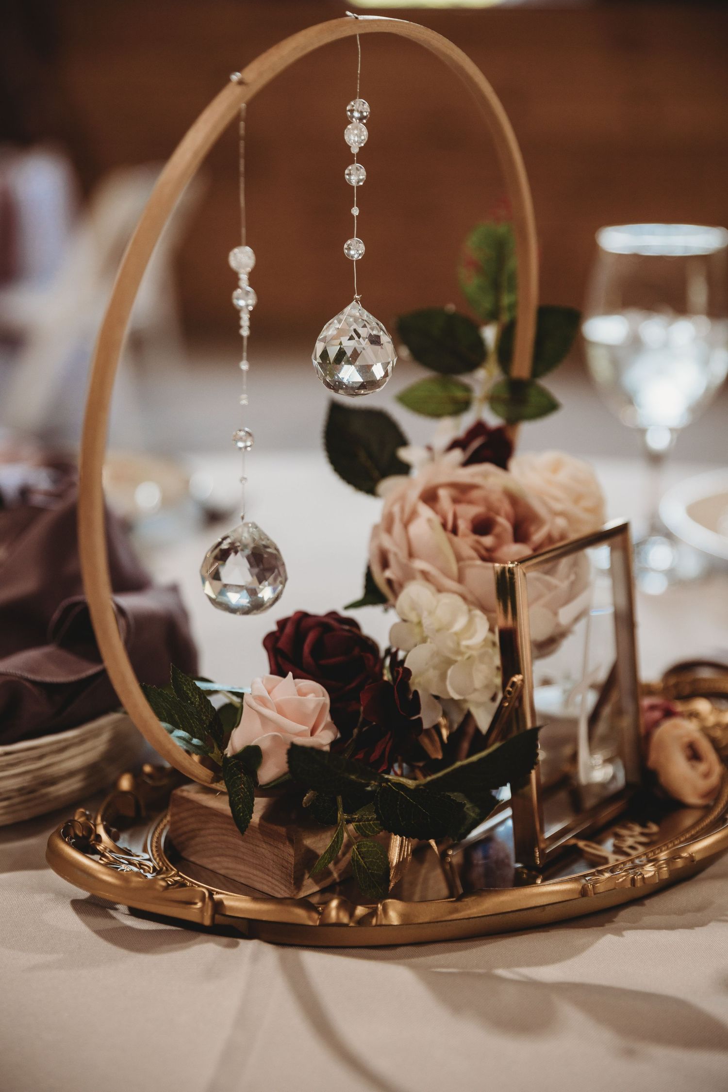 Elegant wedding centerpiece with curved arch, hanging crystals and roses on table setting.