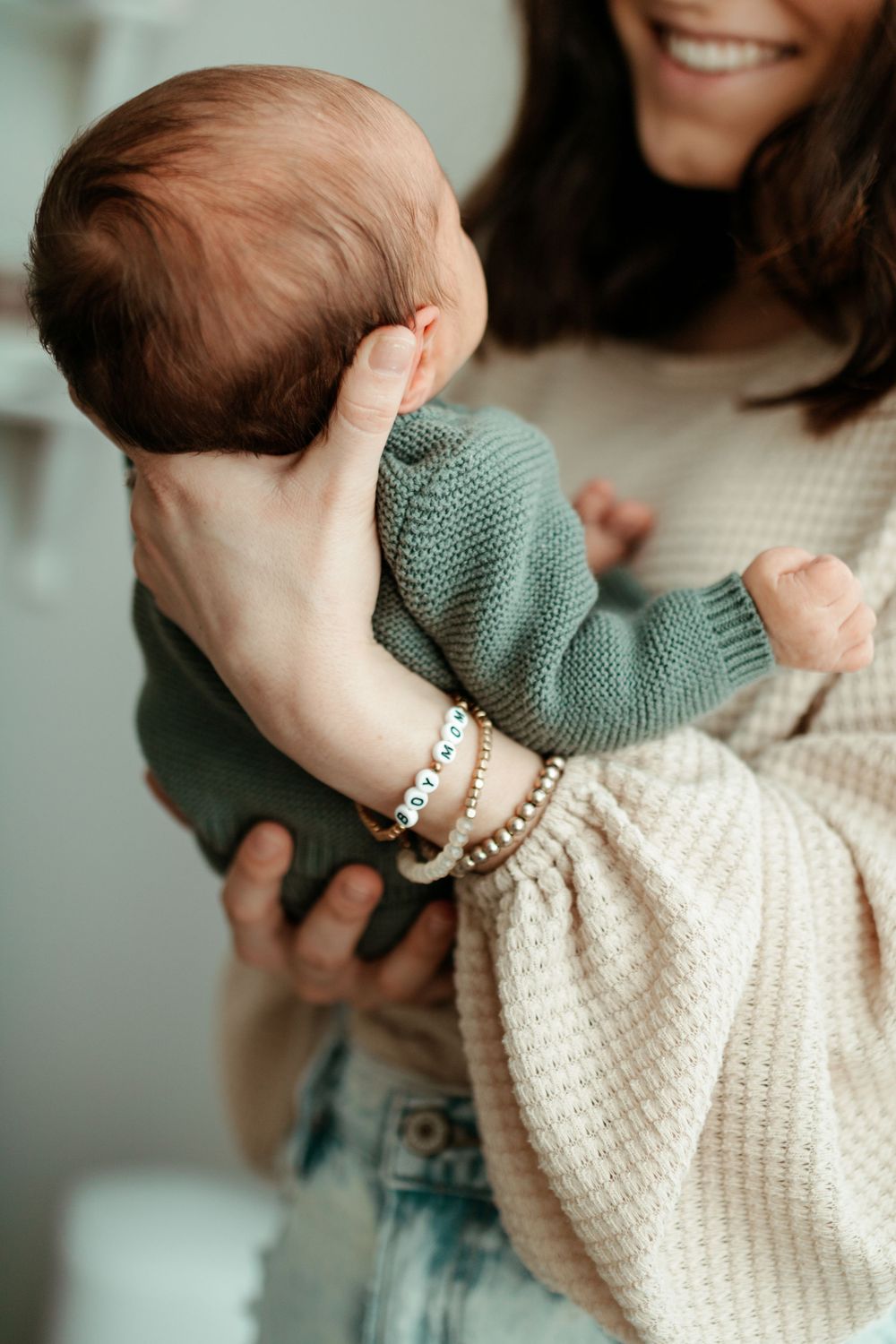 Baby in teal sweater being held against white knit blanket.