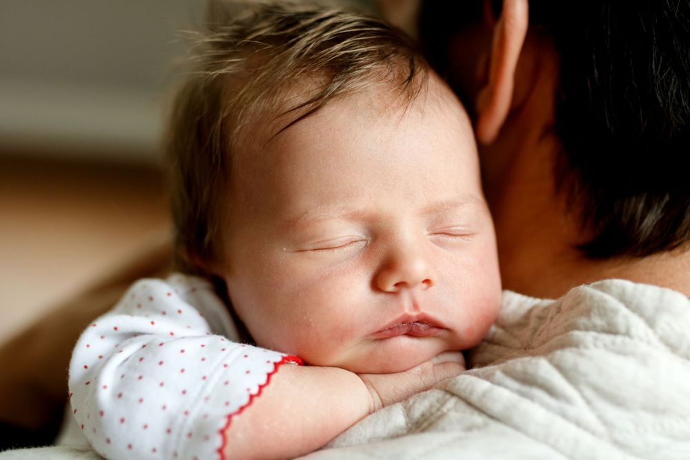 Sleeping infant in polka dot outfit resting peacefully against shoulder.