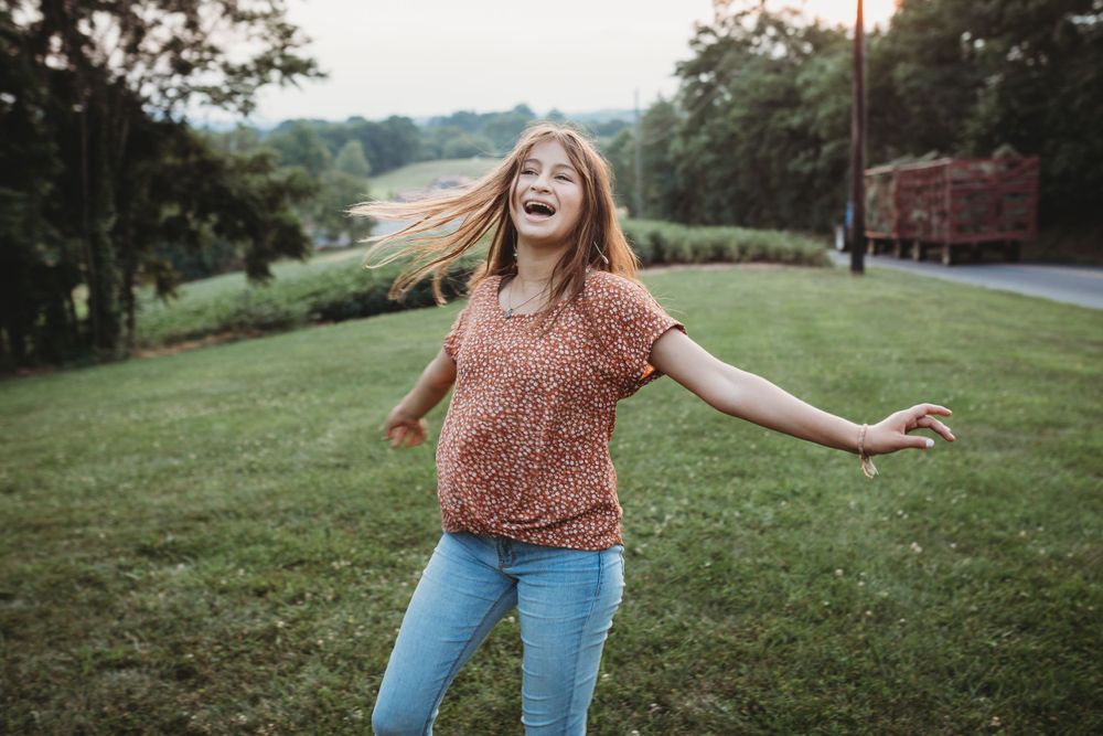 Someone spins and laughs with arms outstretched on a grassy hillside at sunset.