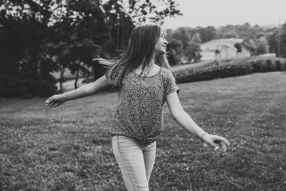 A black and white capture of someone twirling on a grassy hill with arms outstretched.