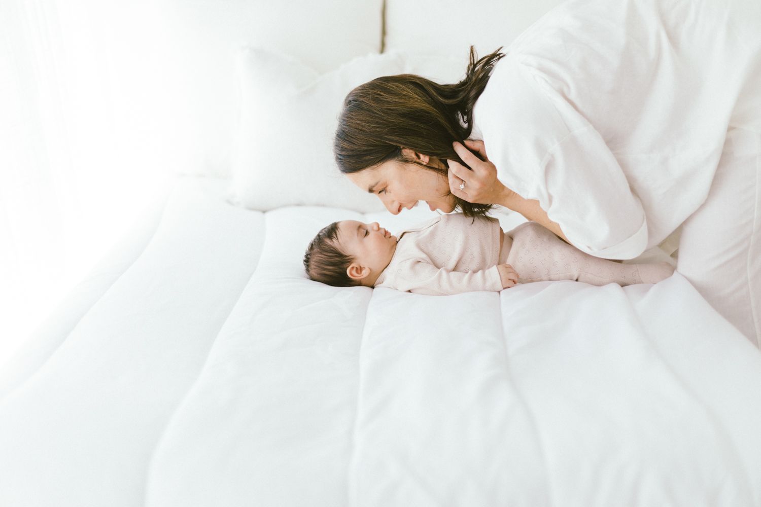 Tender moment between caregiver and baby on white bedding.