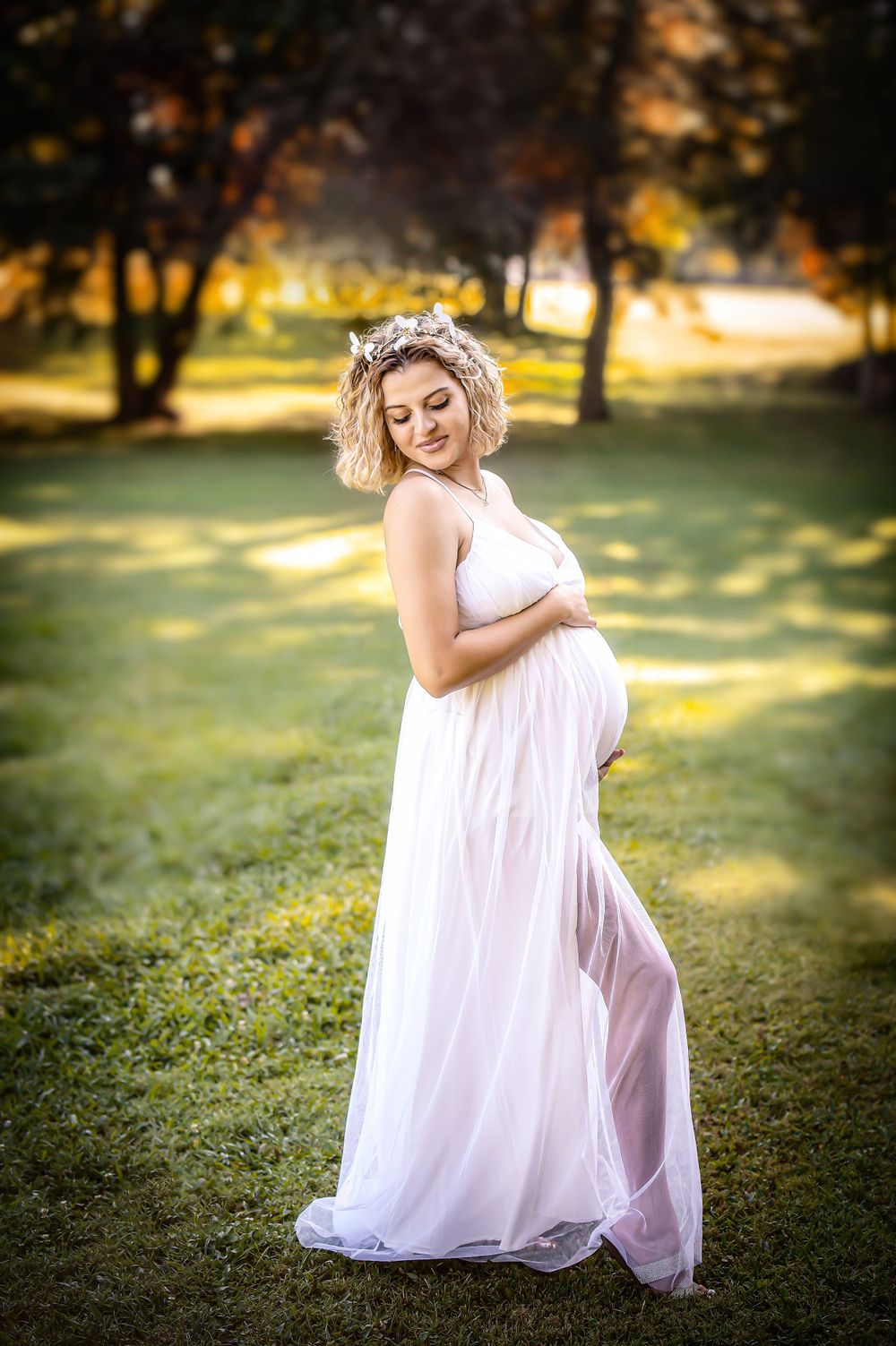 Ethereal maternity portraits in a flowing white dress during golden hour in a garden setting.