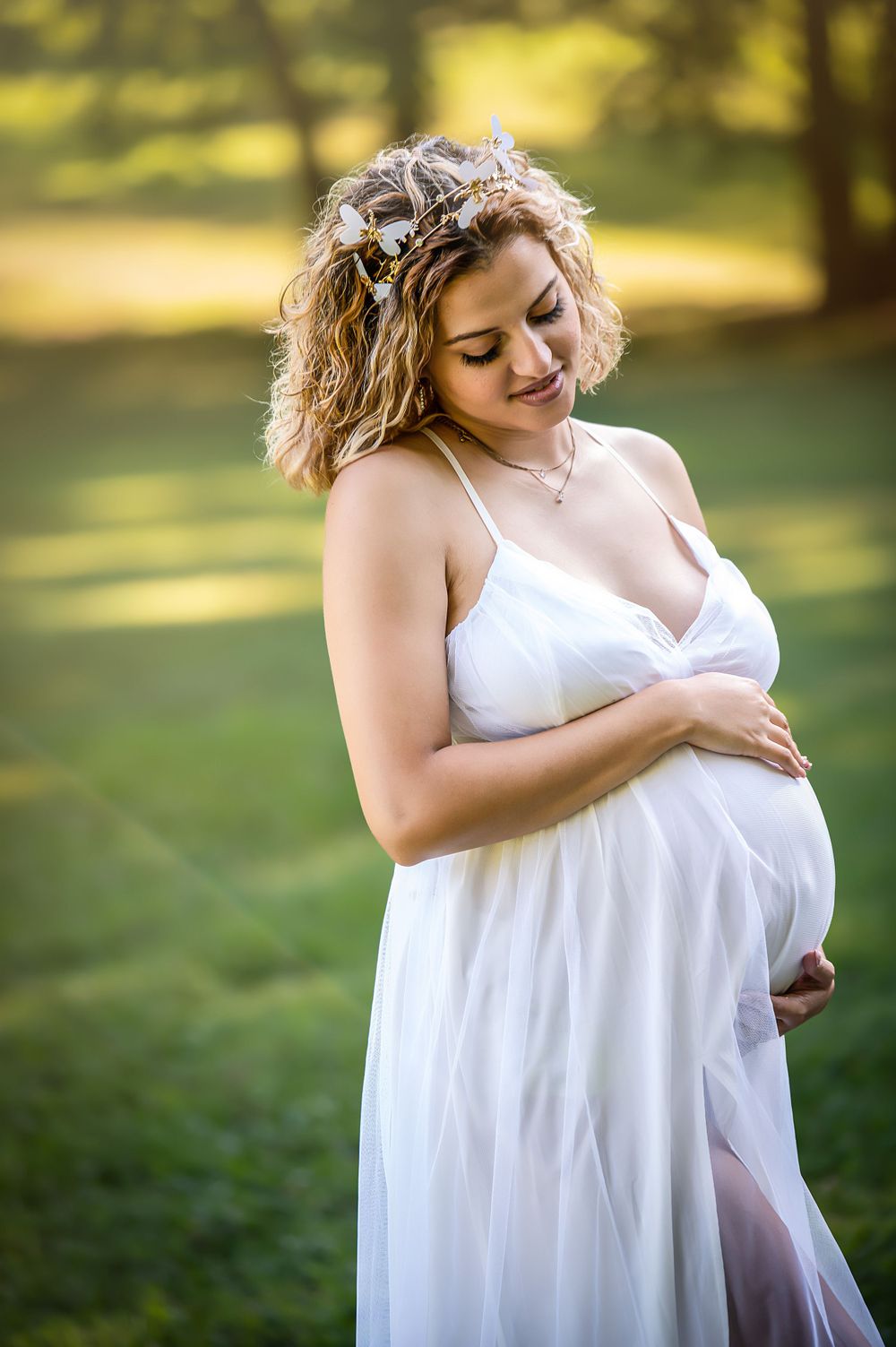 Artistic maternity photos featuring soft white fabric and natural sunlight in a park.
