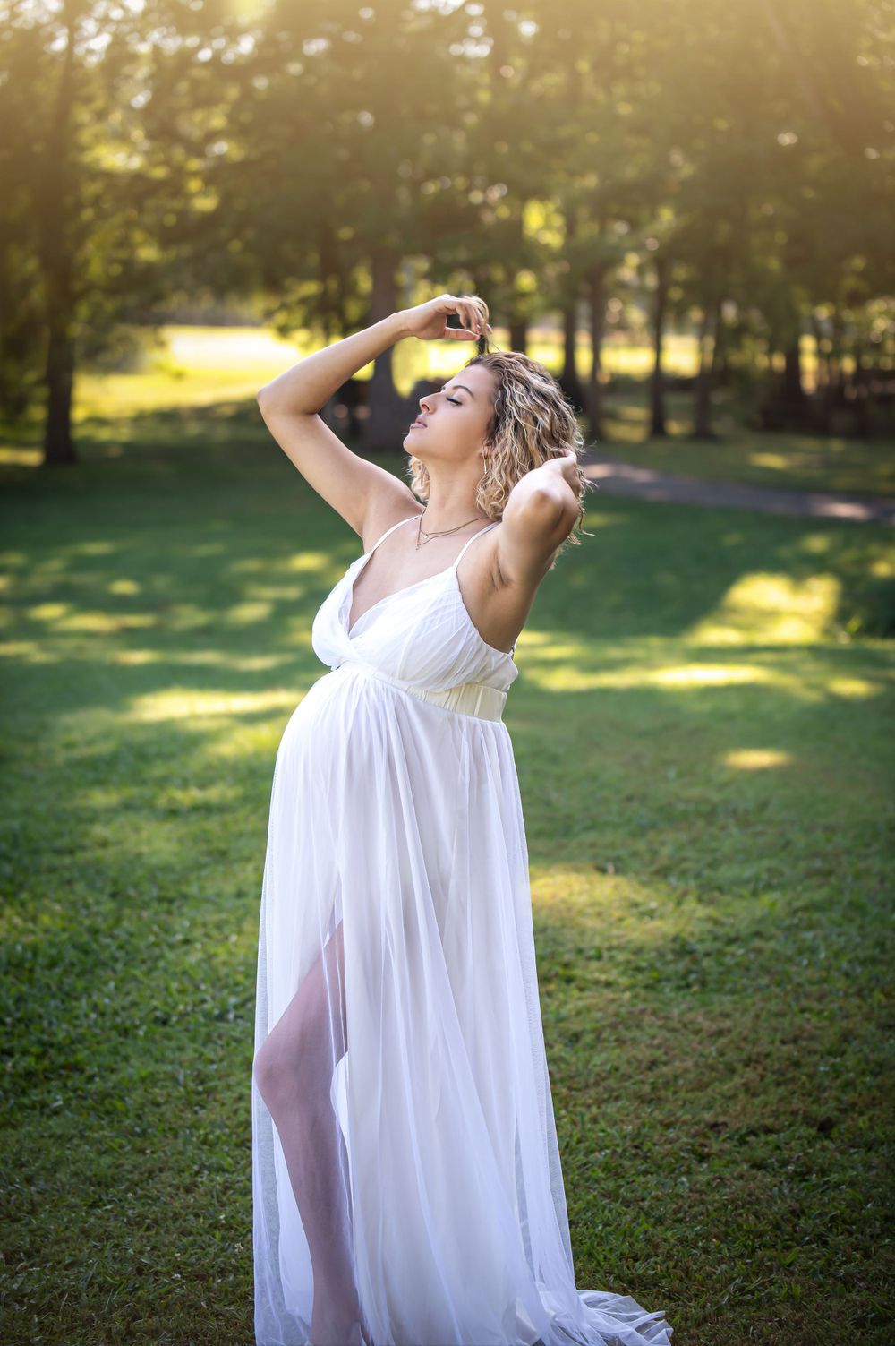 Dreamy maternity portraits with dramatic poses in a sunlit outdoor garden setting.