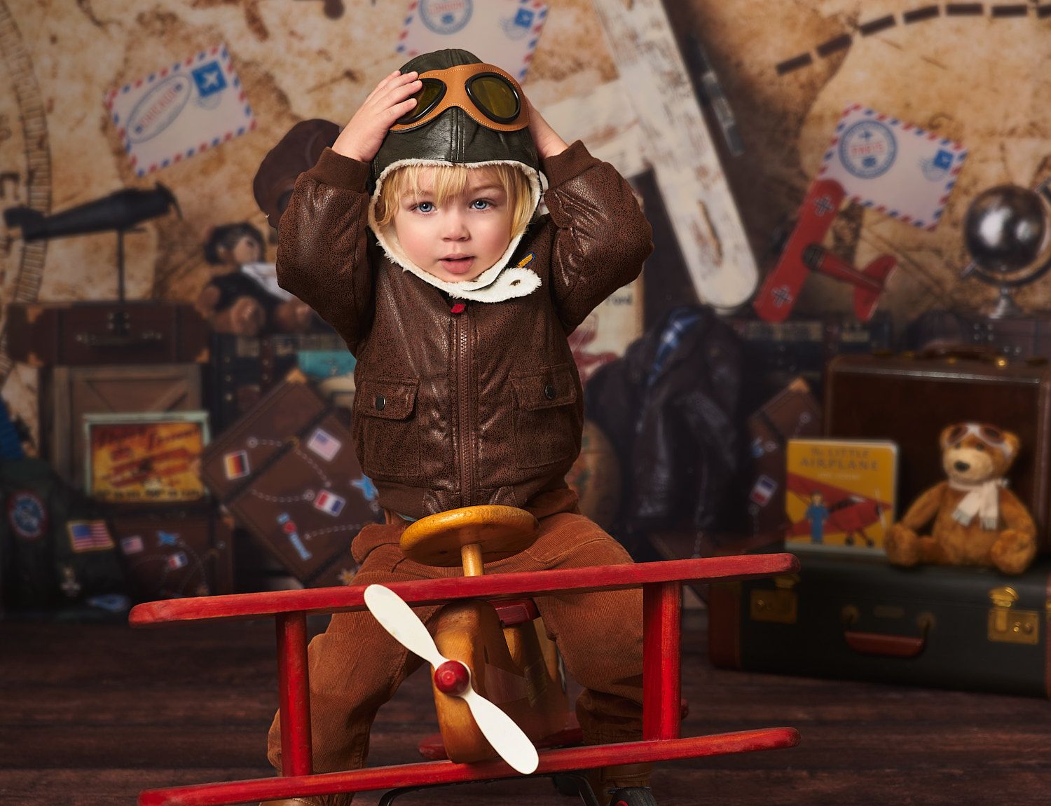 Toddler boy in bomber jacket and hat on vintage wooden airplane