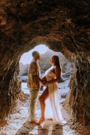 Maternity photography session inside a scenic beach cave with natural lighting.