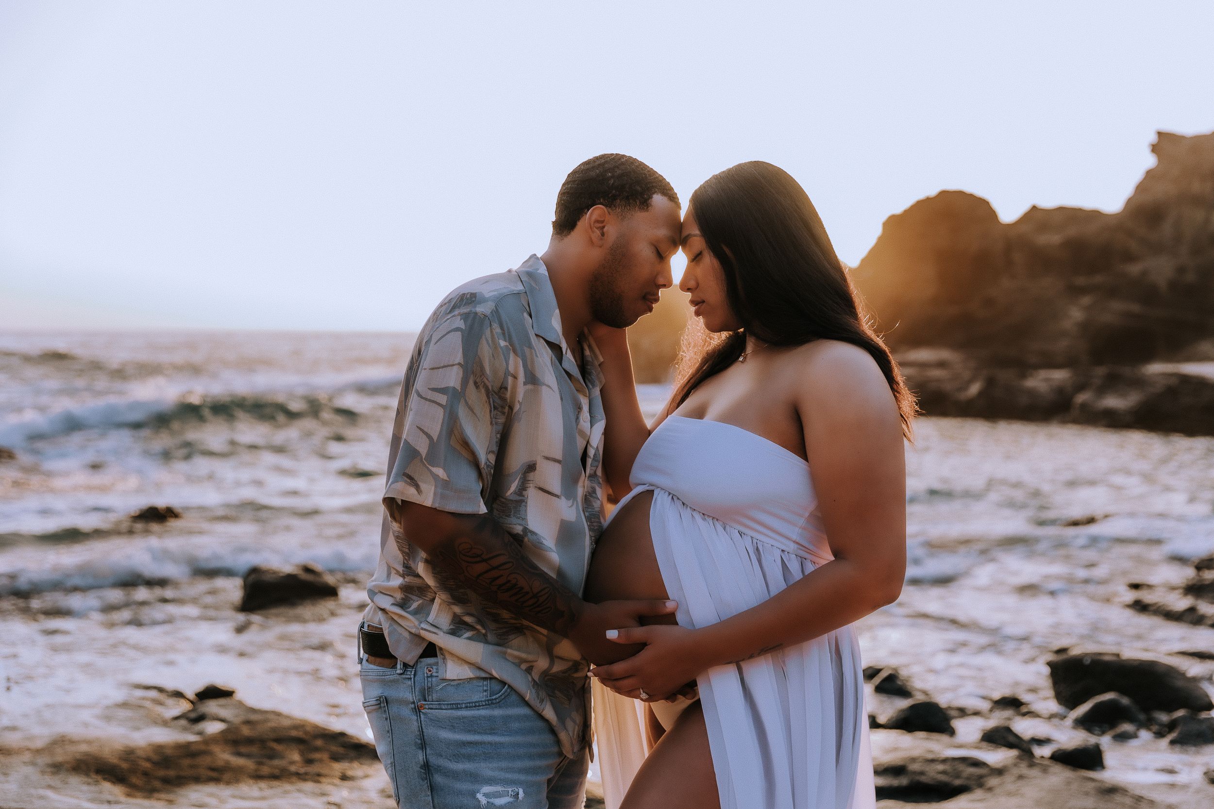 Romantic couple sharing intimate moments on rocky beach during photo session.