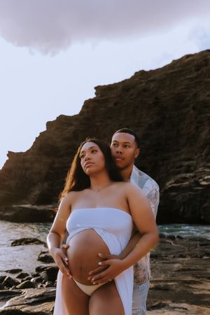 Intimate maternity photos captured against dramatic coastal cliffs during golden hour.