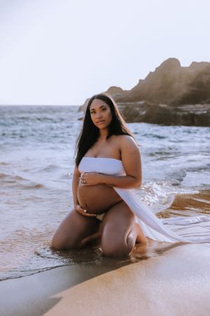 Artistic maternity photos taken at the ocean's edge with waves and rocks.