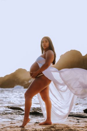 Dramatic maternity beach photos with flowing white fabric at golden hour.