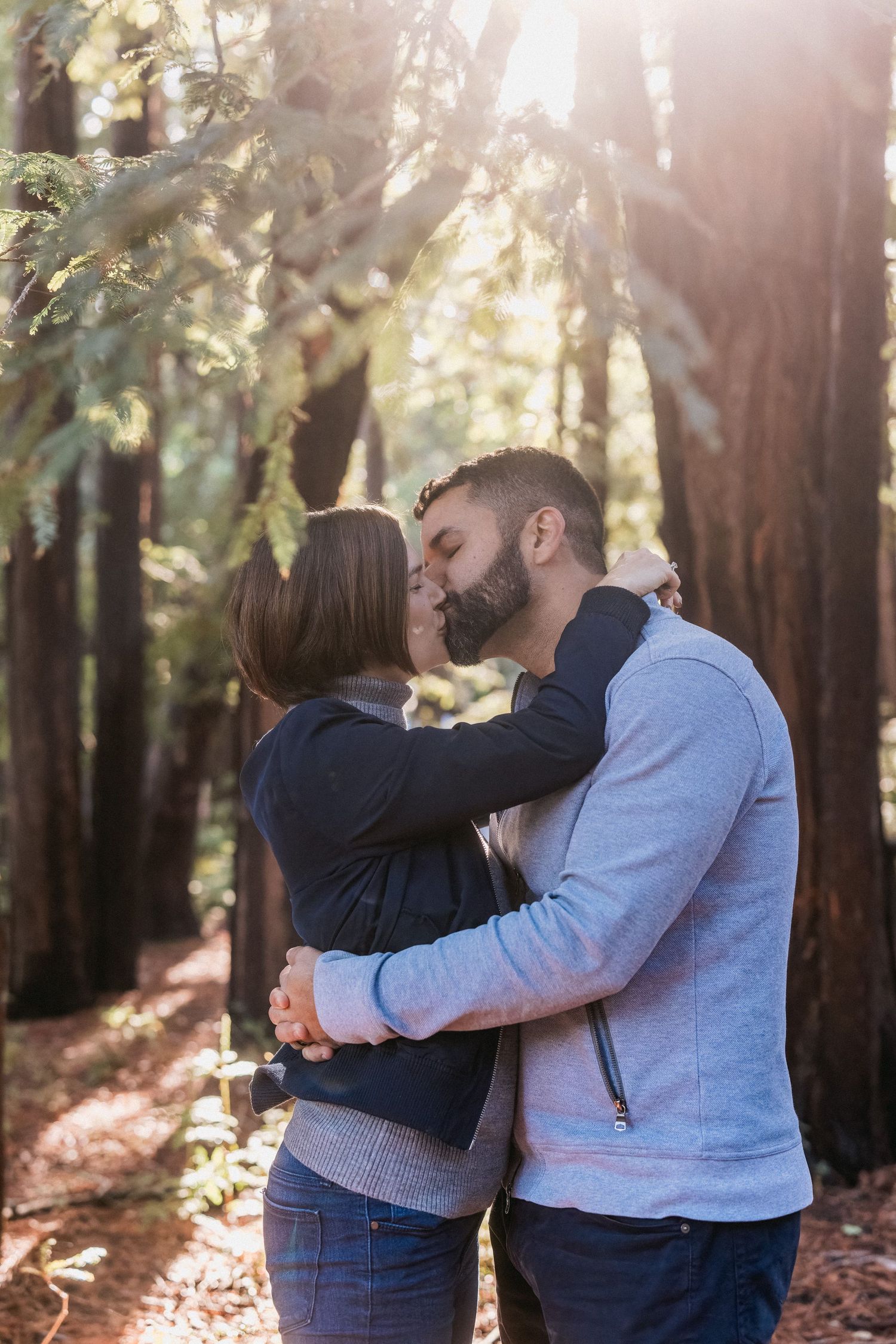 A couple sharing an intimate embrace in a sunlit redwood forest.