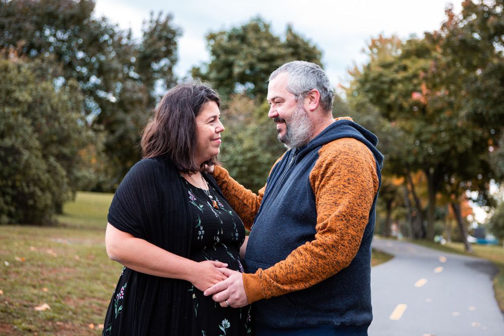Couple laughs together on autumn path surrounded by trees.