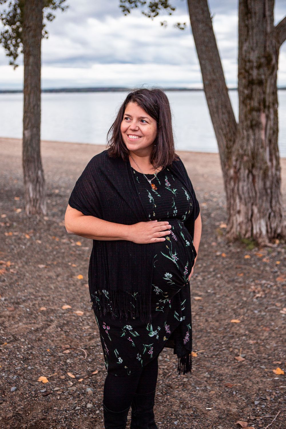 Woman in floral dress smiles by lakeside on autumn day.