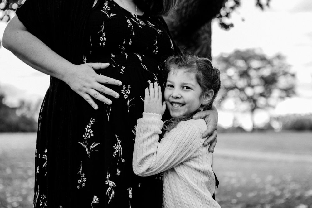 Young child hugs expectant mother's belly in black and white portrait.