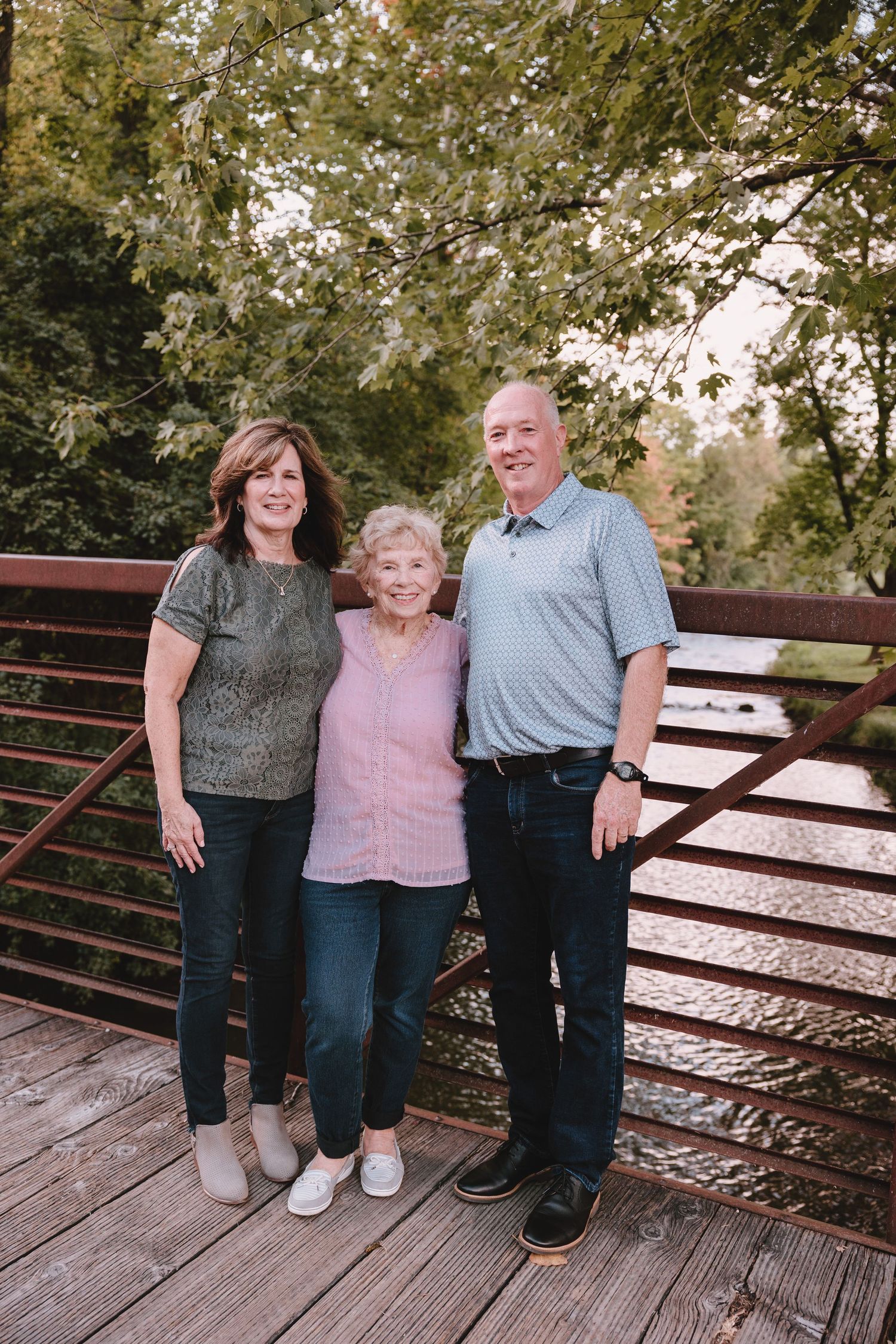 Three people standing together on wooden deck for family photo.