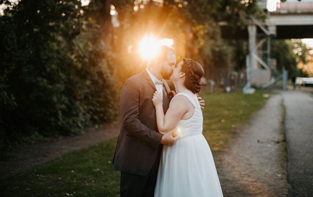 Bride and groom sharing a kiss at golden hour with sunburst glowing behind them.