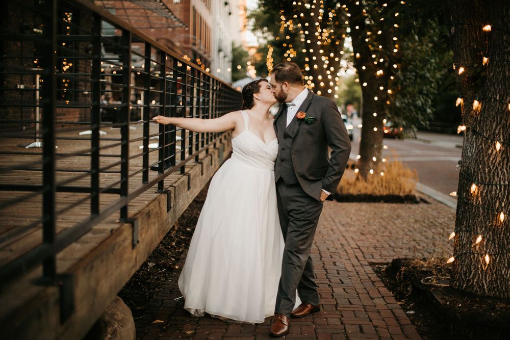 Bride and groom walk along a charming brick pathway lined with warm twinkling fairy lights at dusk.