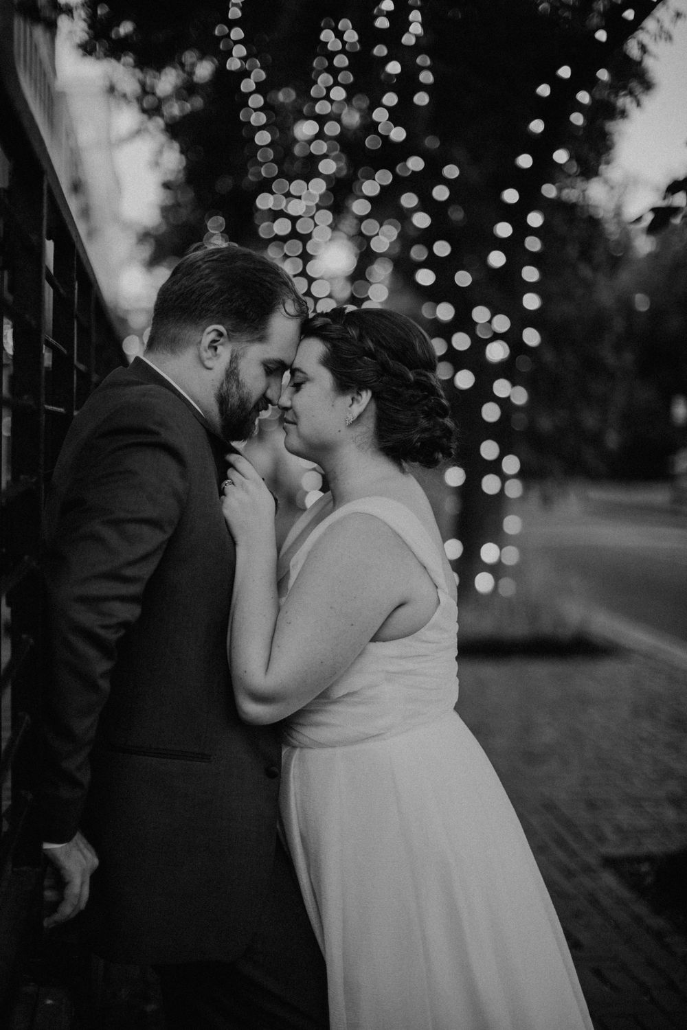 Black and white portrait of bride and groom sharing an intimate moment surrounded by bokeh fairy lights.