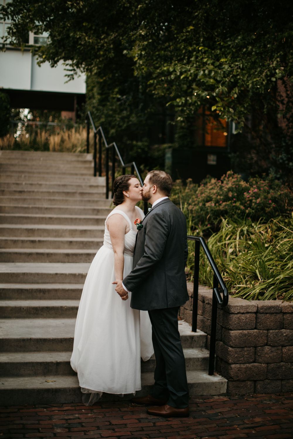 A bride and groom share a romantic kiss on stone steps surrounded by lush greenery on their wedding day.