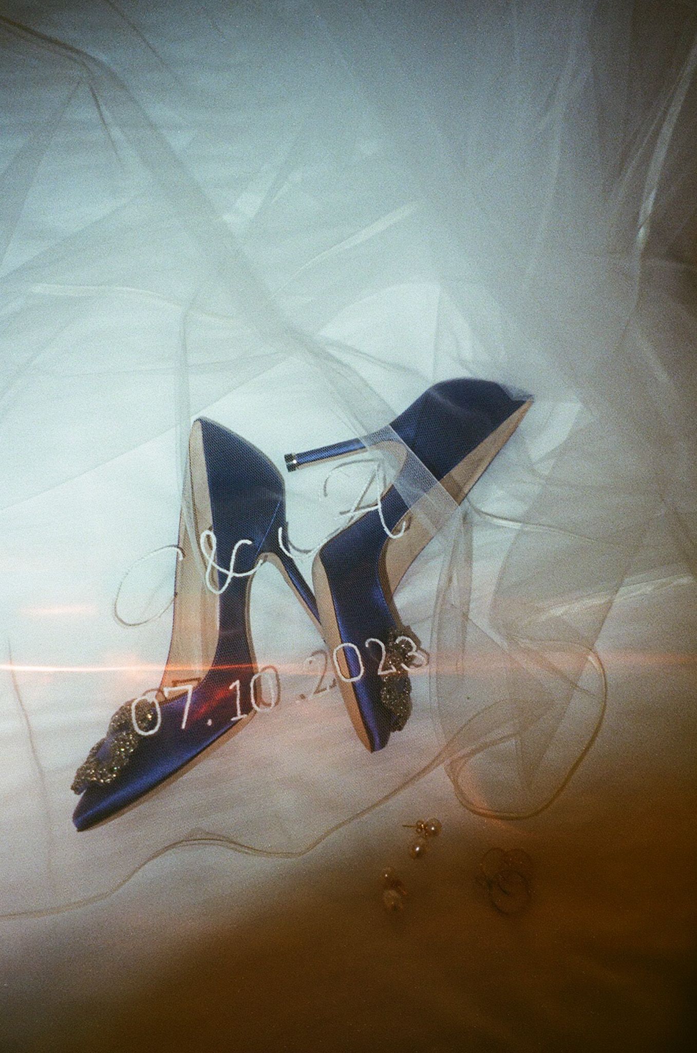 Navy blue wedding shoes photographed through sheer fabric with date text overlay.